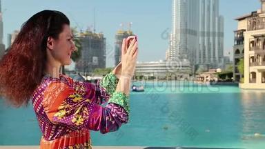 漂亮的女人站在蓝色游泳池附近，在他的智能手机上拍照